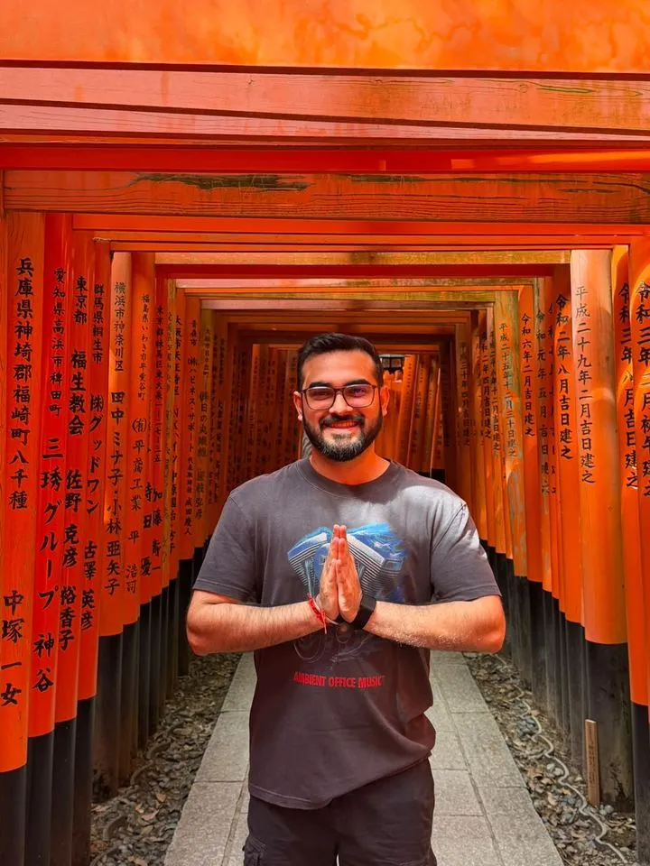 Sidhant smiling with his hands together in a tunnel of orange torii gates